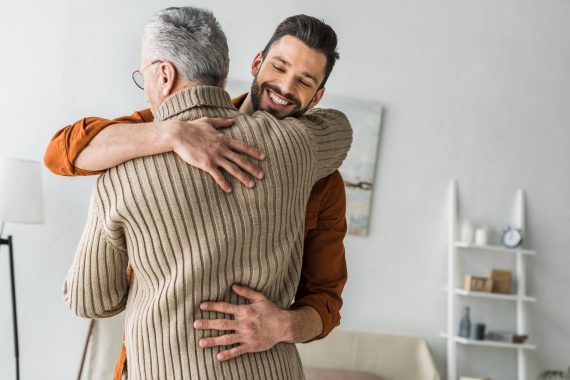 happy bearded man smiling while hugging elder father at home